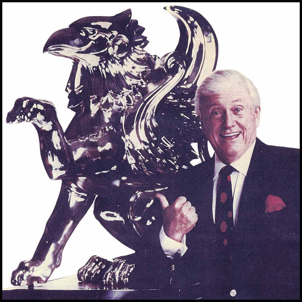 photo of Merv Griffin standing next to a griffin sculpture with a bronze patina