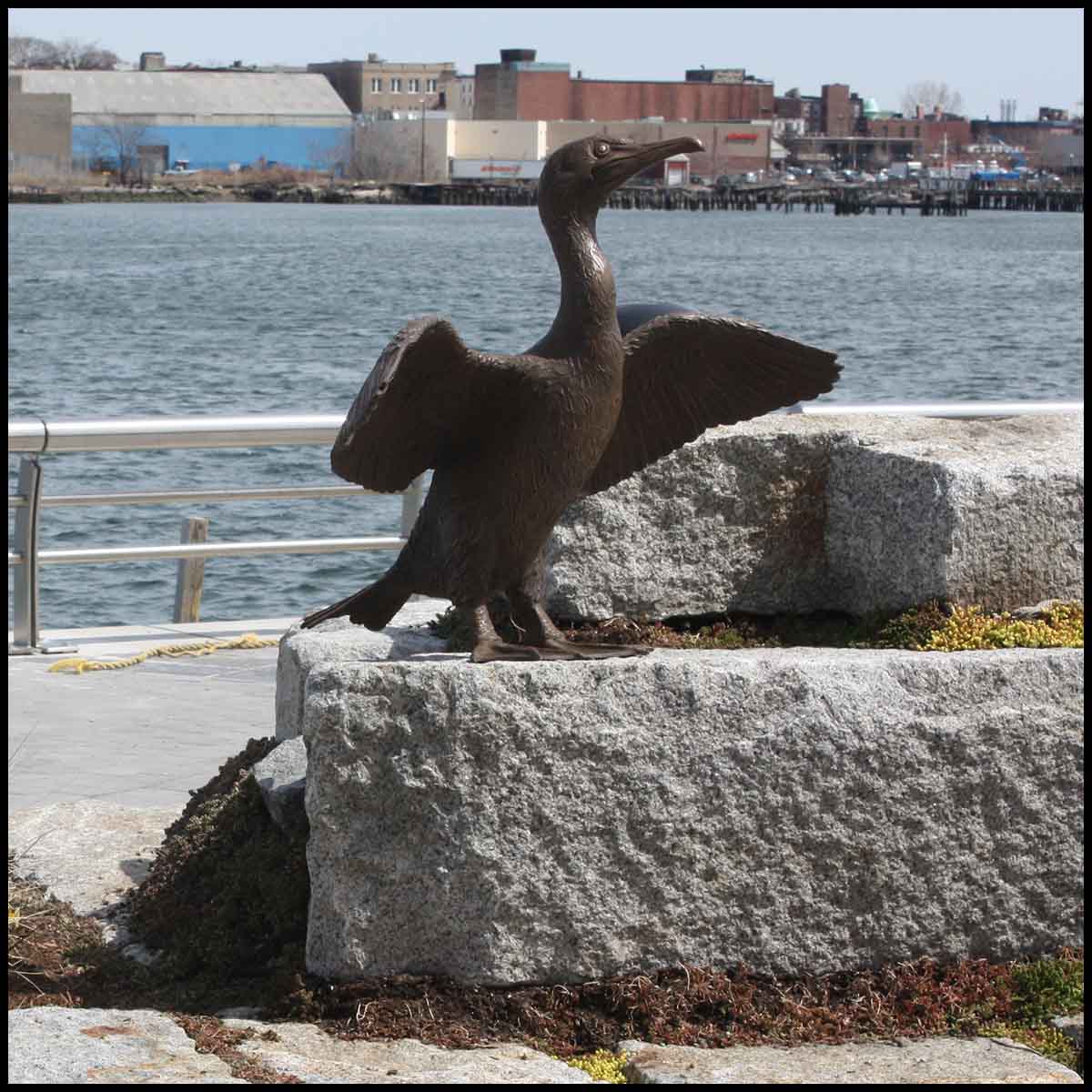 photo of bronze sculpture of cormorant with wings open on low stone block