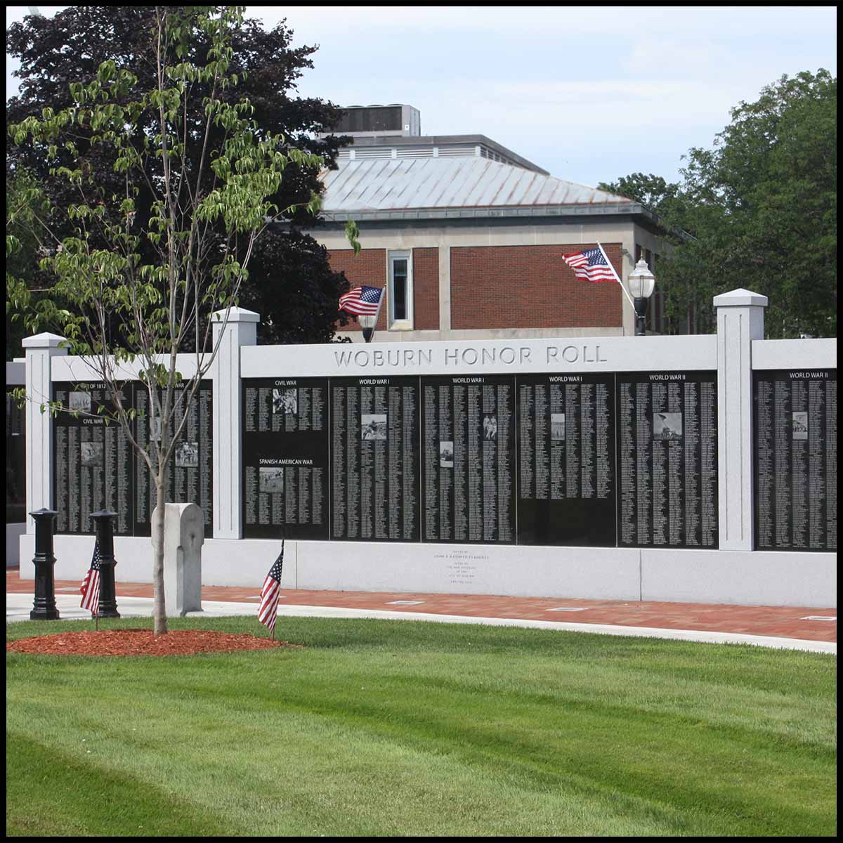 photo of black and gray granite monument in form of a wall in city green with building and trees behind