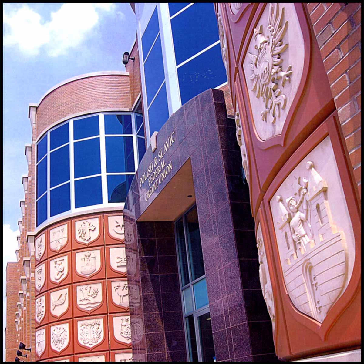 photo of entrance of stone and brick building with rounded tower-like elements and a series of white shields sculpted in relief set in brick-colored squares