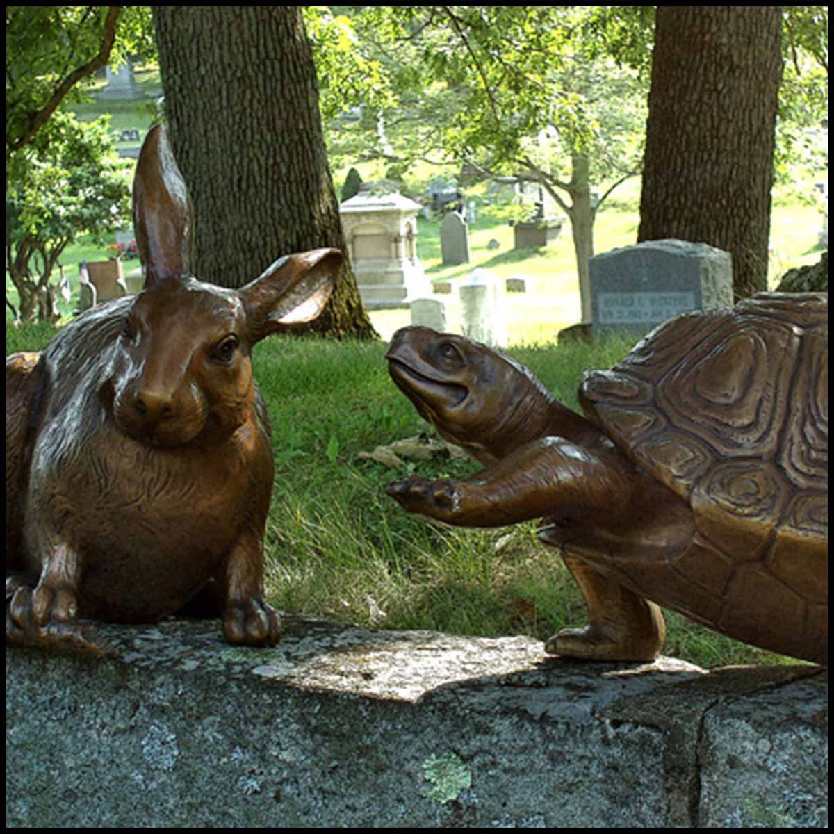 photo of bronze rabbit sculpture and bronze turtle sculpture sitting on a rock wall with grass and trees in the background
