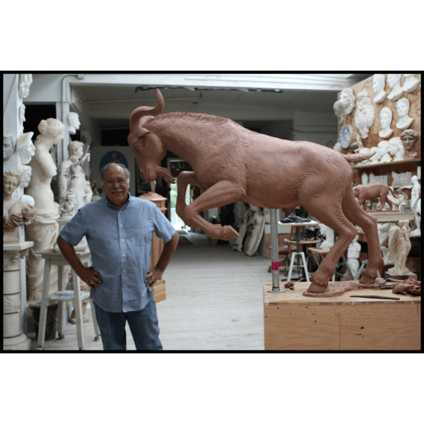 photo of sculptor Robert Shure with clay model of sculpture of goat charging forward with front legs raised off pedestal