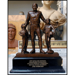 photo of bronze-colored sculpture of Rob Burton in football gear with a child on either side atop a black stone base with a plaque