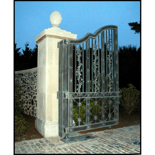 photo of one half of ornamental bronze entrance gate with stone pillars and shrubs to the side